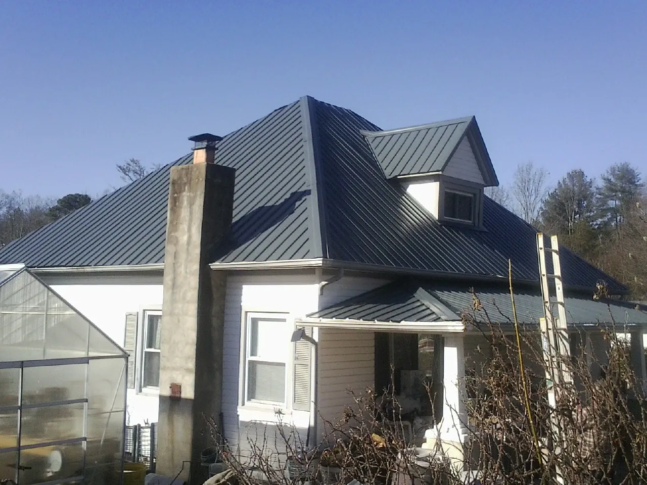 Dark blue standing seam metal roof on a white farmhouse with dormer — Slate & Tile Roof Repair by Roofing Brothers in Charleston