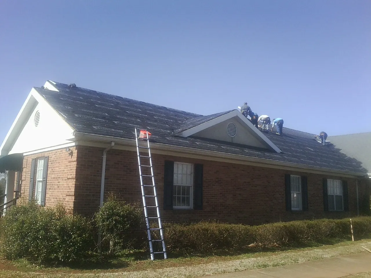 Crew tearing shingles off a brick ranch roof with a ladder set — Emergency Roof Repair work by our crew in Charleston