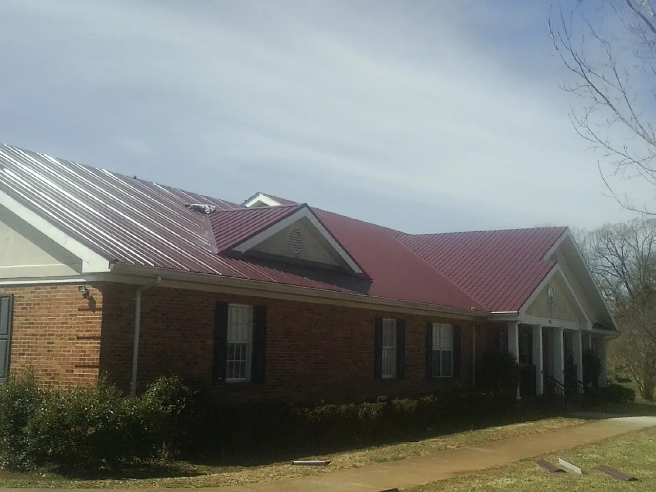 Red metal roof with gabled entries on a long brick building, from a Hail Damage Roof Repair job in Charleston